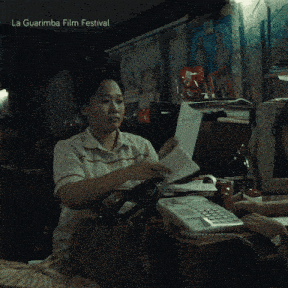a woman sitting at a desk holding a piece of paper with the words la guarimba film festival below her