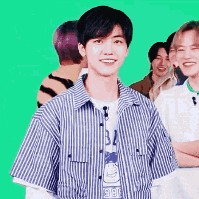 a young man in a striped shirt is smiling in front of a group of young men .