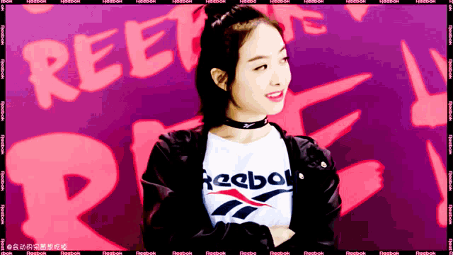 a woman wearing a reebok t-shirt is standing in front of a purple background