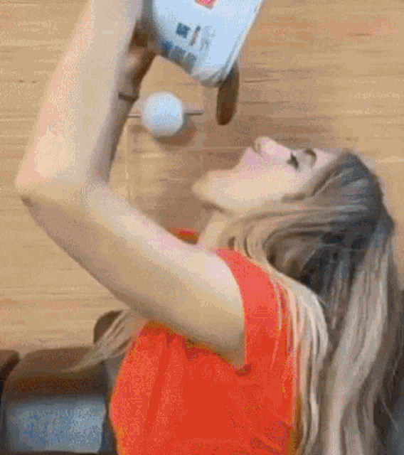 a woman in an orange shirt is drinking from a bottle of milk