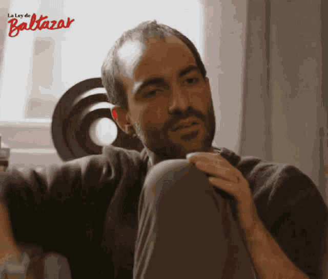 a man with a beard is sitting in front of a window with the words la ley de baltazar on the bottom
