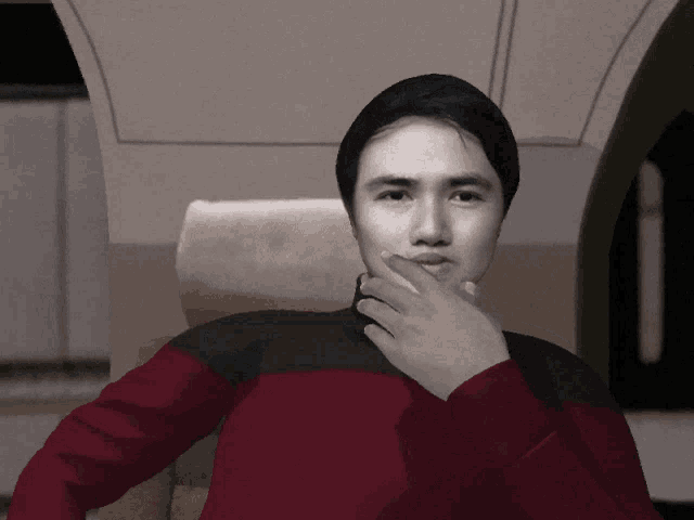 a man in a red and black shirt holds his hand to his face