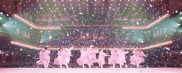 a group of people are dancing on a stage with petals falling around them