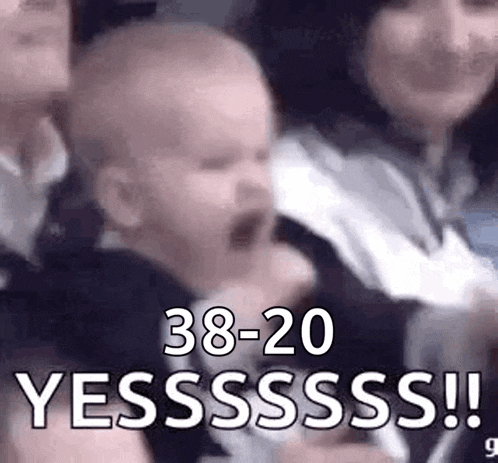 a baby is screaming in a crowd of people while a woman holds it .