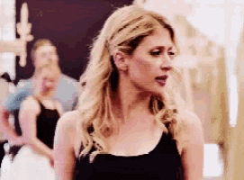 a woman in a black tank top is standing in front of a crowd of people .