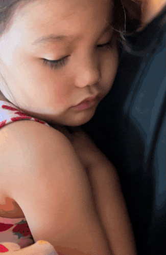 a little girl with her eyes closed is being held by a person