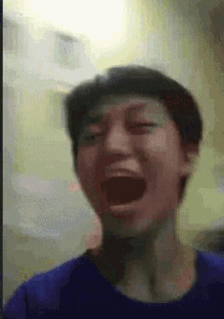 a man in a blue shirt is screaming with his mouth open