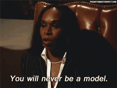 a woman in a suit and white shirt is sitting in a chair and says " you will never be a model "