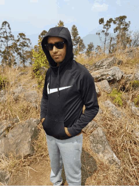 a man wearing a nike hoodie and sunglasses stands in a field