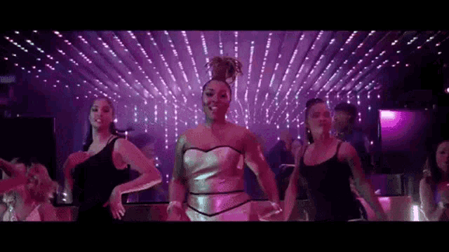 a group of women are dancing in a club with purple lights on the ceiling .