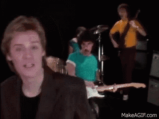 a group of men are playing guitars in a dark room while a woman sings .