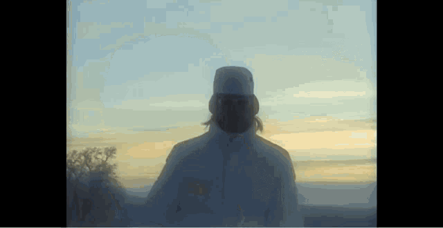 a man in a white coat and hat is standing in the snow .