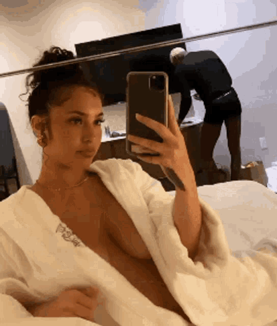 a woman in a white robe is taking a picture of herself in a mirror