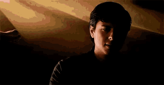 a young boy is standing in the dark with the sun shining through the window behind him .