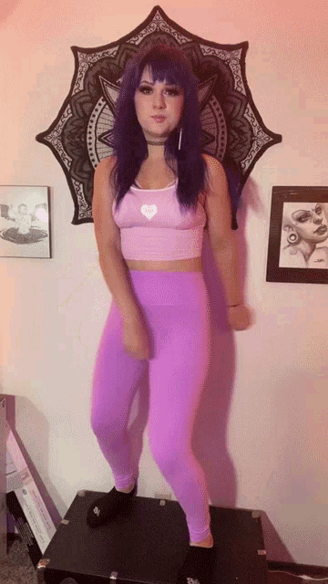 a woman with purple hair wearing purple leggings and a pink top with a heart on it