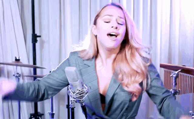 a woman singing into a microphone with her arms outstretched in front of a drum set