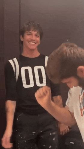 a man in a black shirt with the number 00 on it is standing next to another man in a white shirt .