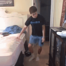 a boy in a black shirt and blue shorts stands on a bed