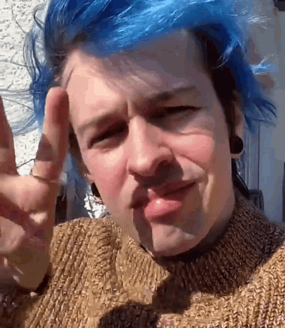 a man with blue hair is wearing a brown sweater and giving the peace sign