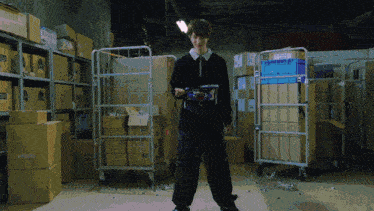 a man is standing in a warehouse with boxes and carts and a blue container that says ' g ' on it