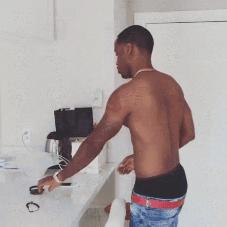 a man without a shirt is standing in front of a desk in a room .