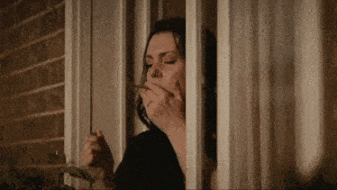 a woman smoking a cigarette in front of a window