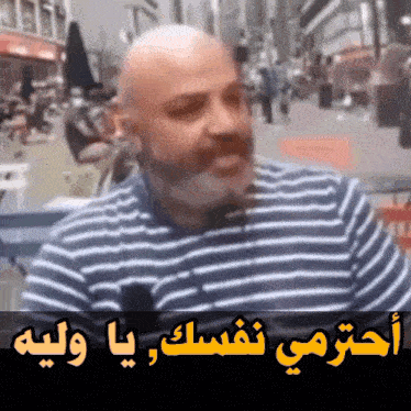 a bald man with a beard is wearing a striped shirt with arabic writing on it
