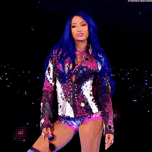 a woman with blue hair is standing on a stage wearing a colorful outfit .