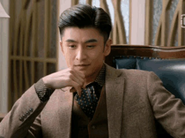 a man in a suit and tie is sitting in a chair with his hand on his chin