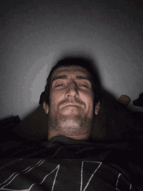 a man with a beard is laying down with his eyes closed and wearing a shirt that says " la " on it