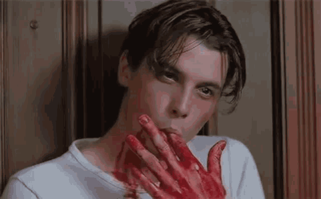 a man is licking his bloody hand while standing next to a door .