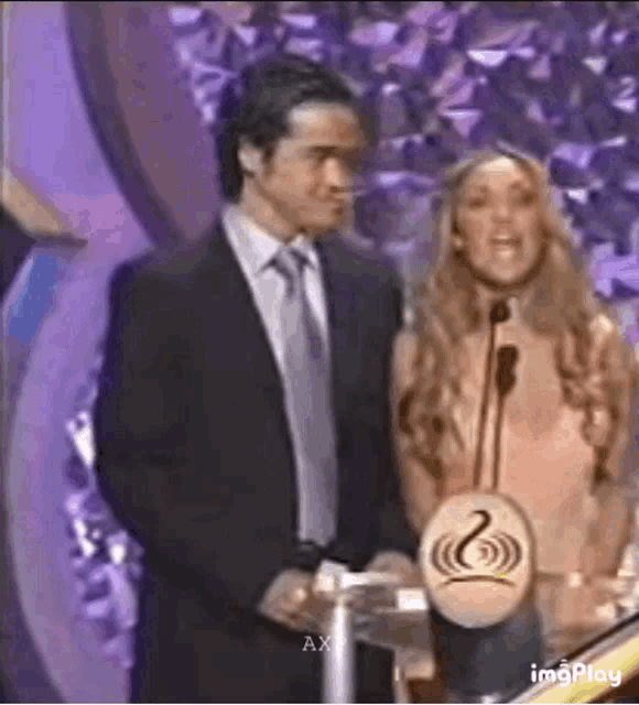 a man in a suit and tie is standing next to a woman holding a trophy .