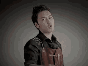 a young man wearing a black shirt and an apron is making a funny face .
