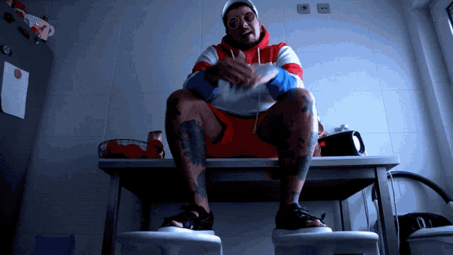 a man in a red white and blue hoodie sits at a table with his legs crossed