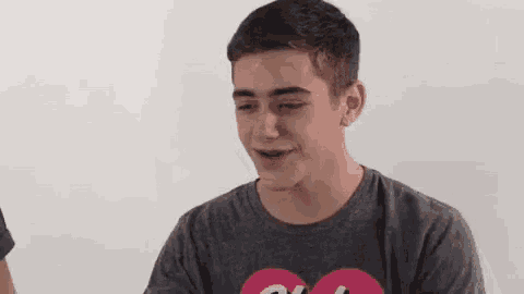 a young man wearing a gray t-shirt with a pink heart on it is smiling .