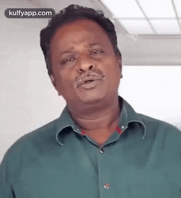 a man in a green shirt is making a funny face while standing in a room .