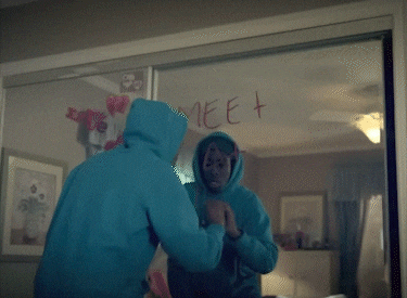 a person in a blue hoodie looking at their reflection in a mirror