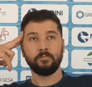 a man with a beard holds his finger to his forehead in front of a wall with logos for gini and gesa