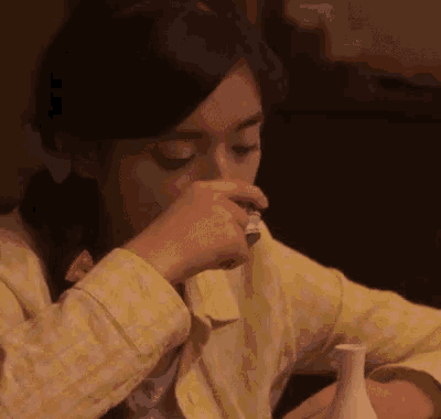 a woman is sitting at a table drinking from a small cup .
