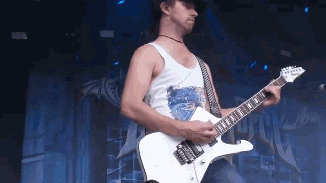 a man in a white tank top is playing a guitar