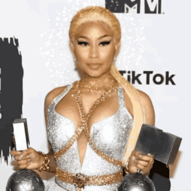 a woman in a silver dress is holding two trophies in front of a tiktok logo
