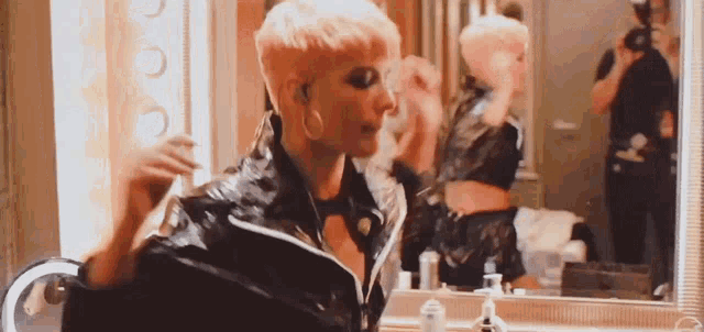 a woman is standing in front of a mirror in a bathroom applying makeup .