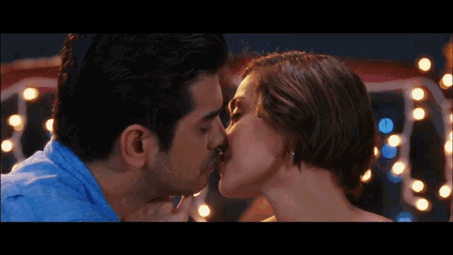 a man and a woman are kissing in front of christmas lights