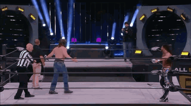 a wrestler is standing in the middle of a ring with a referee and a sign that says all elite wrestling