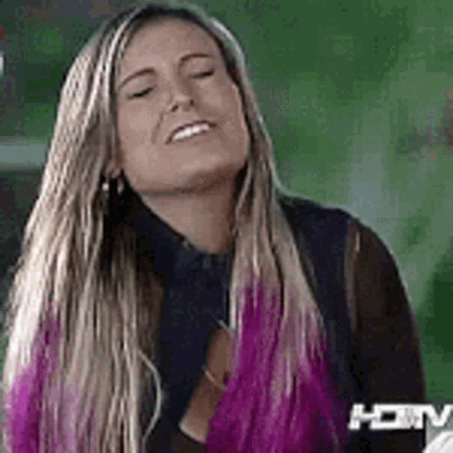 a woman with long blonde hair and pink highlights is smiling and making a funny face .