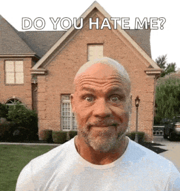 a bald man with a beard is making a funny face in front of a brick house and says do you hate me .