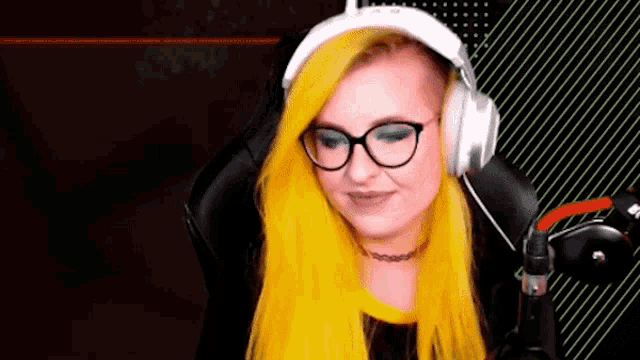 a woman with bright yellow hair and glasses is wearing headphones and sitting in a chair .
