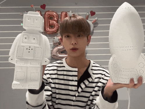 a boy in a striped shirt is holding a robot and a rocket in his hands