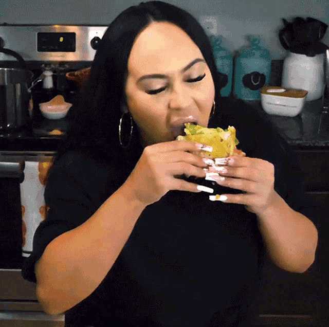 a woman with white nails is eating a sandwich in front of a stove