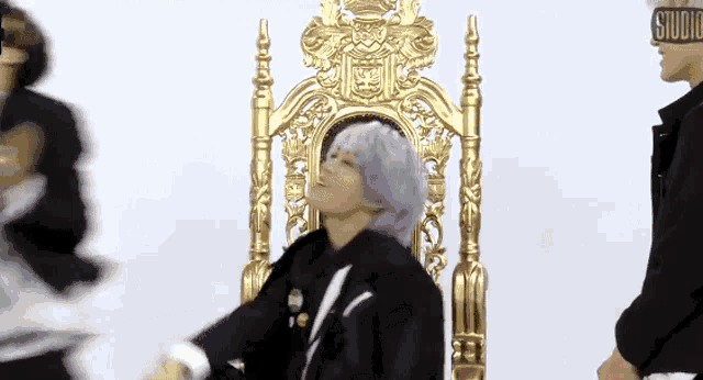 a man with purple hair is sitting on a gold throne and making a funny face .